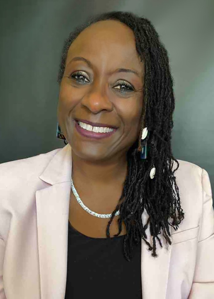 Image of Rozella Kennedy, a Black woman with shoulder length twists, smiling in a pink blazer and black top with a necklace and earrings.